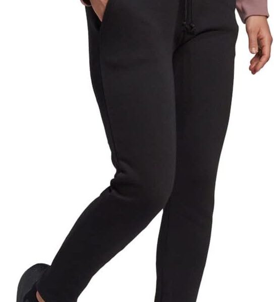 A woman wearing Adidas slim-fit black jogger pants paired with black sneakers and a light pink sweatshirt.