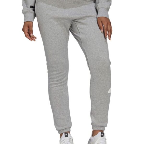 Adidas women's grey sweatpants with a tapered fit, elastic cuffs, and drawstring waistband, paired with white sneakers.