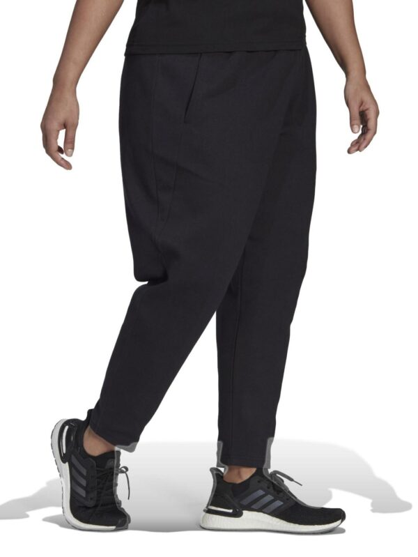 Adidas women's plus-size black jogger pants with a tapered design, shown paired with black Adidas sneakers