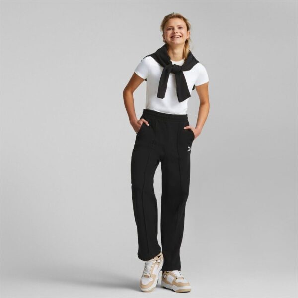 A woman wearing black Puma relaxed-fit pants paired with a white t-shirt and sneakers, showcasing a casual sporty style.