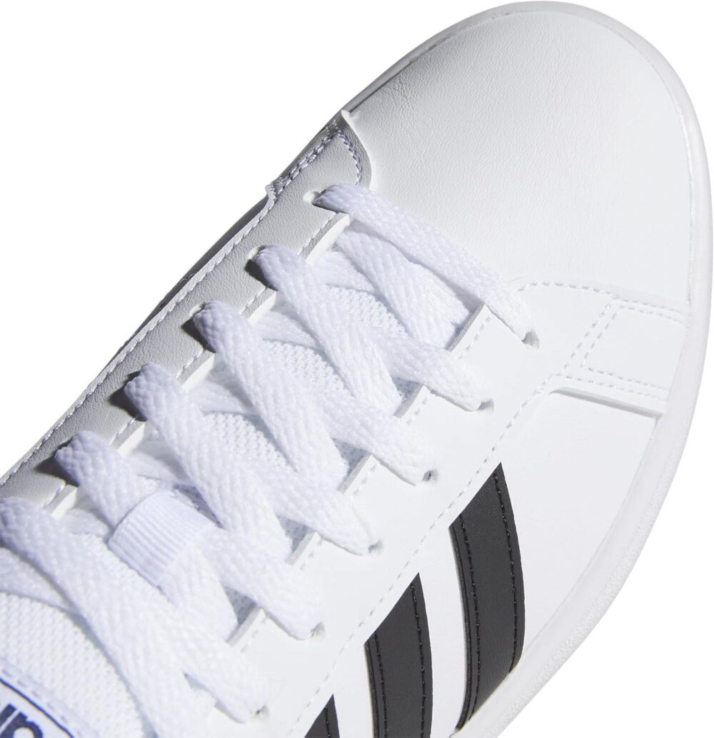 A pair of Adidas men's white sneakers with black stripes, shown on feet with blue joggers, ideal for casual or sporty wear.