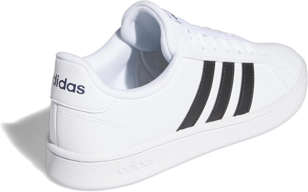 A pair of Adidas men's white sneakers with black stripes, shown on feet with blue joggers, ideal for casual or sporty wear.