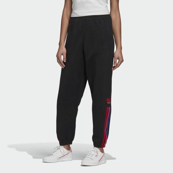 A woman wearing Adidas black track pants with red and blue side stripes, paired with a white top and white sneakers, showcasing a sporty and casual style