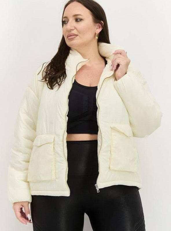 Plus-size woman wearing a cream-colored puffer jacket with a zip-up closure and pockets.