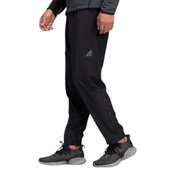 A man wearing Adidas black training pants with a sleek design and subtle branding, paired with black sneakers, perfect for athletic or casual activities.