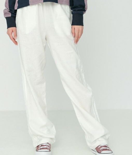 A woman wearing Adidas white wide-leg track pants, paired with a striped top and metallic sneakers, showcasing a relaxed and stylish look.