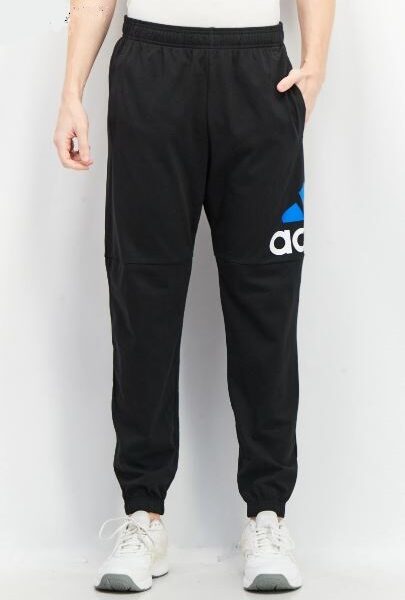 A man wearing Adidas black joggers with a blue and white logo on the leg, paired with white sneakers, ideal for casual and athletic wear