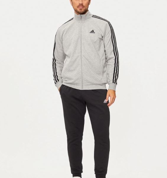 Man wearing an Adidas grey tracksuit jacket with black jogger pants and white sneakers.