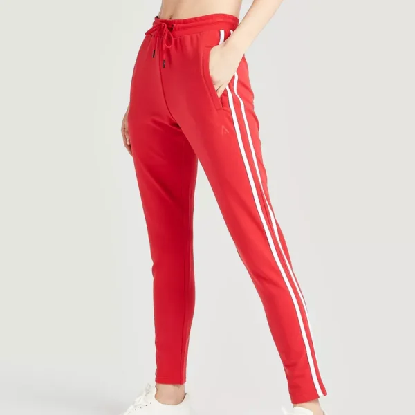 Women's red track pants with white stripes, featuring a logo on the hip.