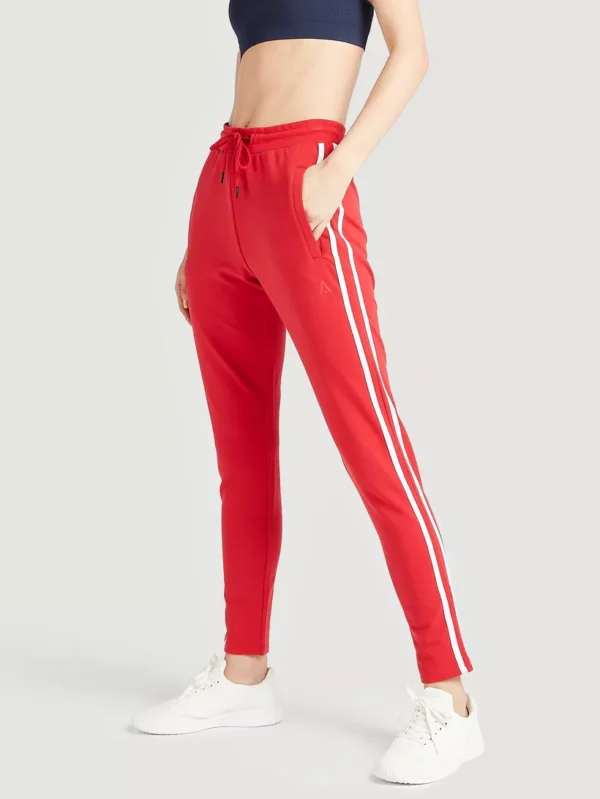 Women's red track pants with white stripes, featuring a logo on the hip.